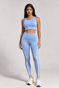 Woman wearing a light blue athletic outfit with white stripes on a plain background